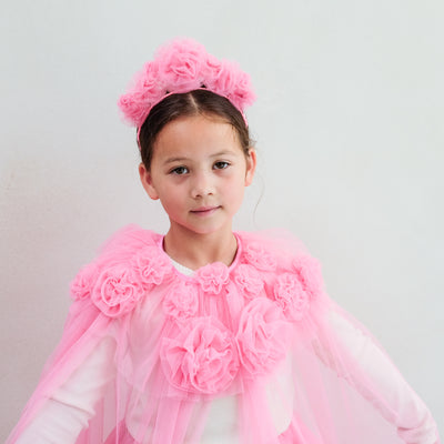 Young girl wearing a pink floral headband and cape against a light grey background