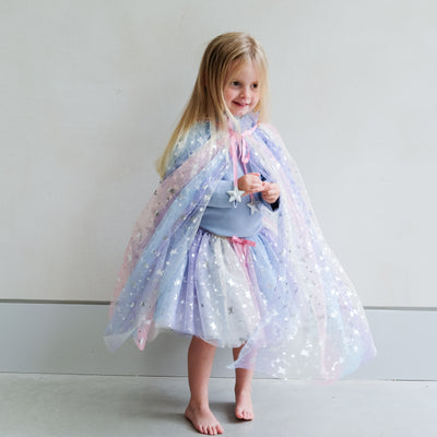 Young girl wearing a colourful star-patterned rainbow cape and tutu against a plain background