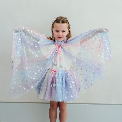 Young girl wearing a star-patterned cape and tutu against a plain background