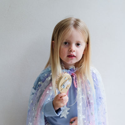 Child holding a wooden unicorn hairbrush against a plain background
