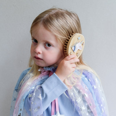 Child holding a wooden unicorn hairbrush against a plain background