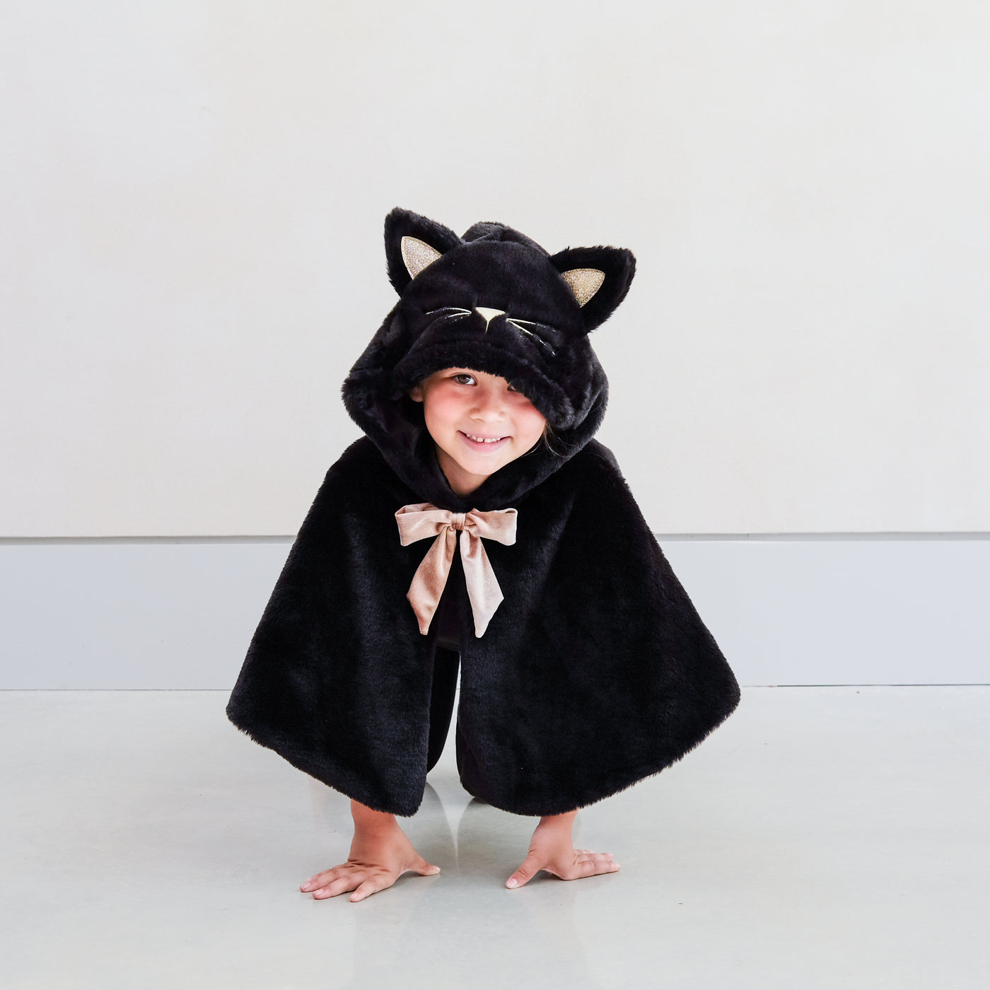 child wearing black fur cat dressing up cape against a plain background