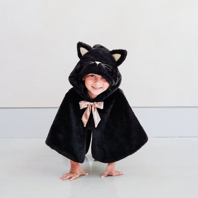 child wearing black fur cat dressing up cape against a plain background