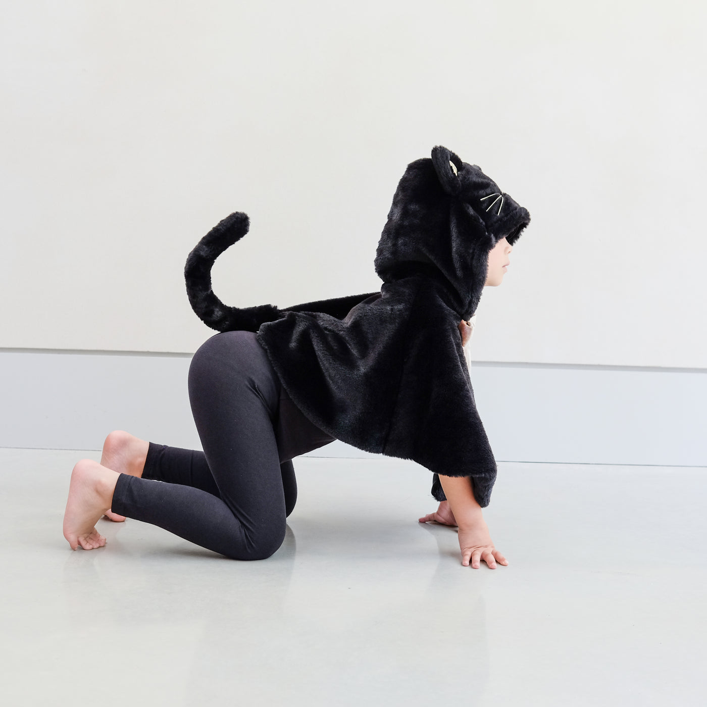 Child wearing black fur cat dressing up cape against a plain background