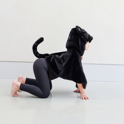 Child wearing black fur cat dressing up cape against a plain background