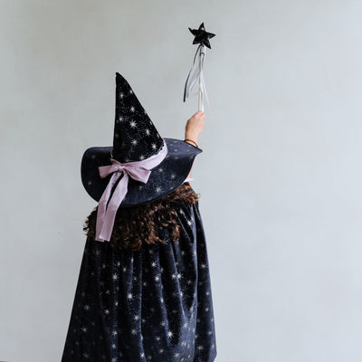 Child in a Agatha velvet black witch costume with a black witches hat and star-patterned cape against a white background
