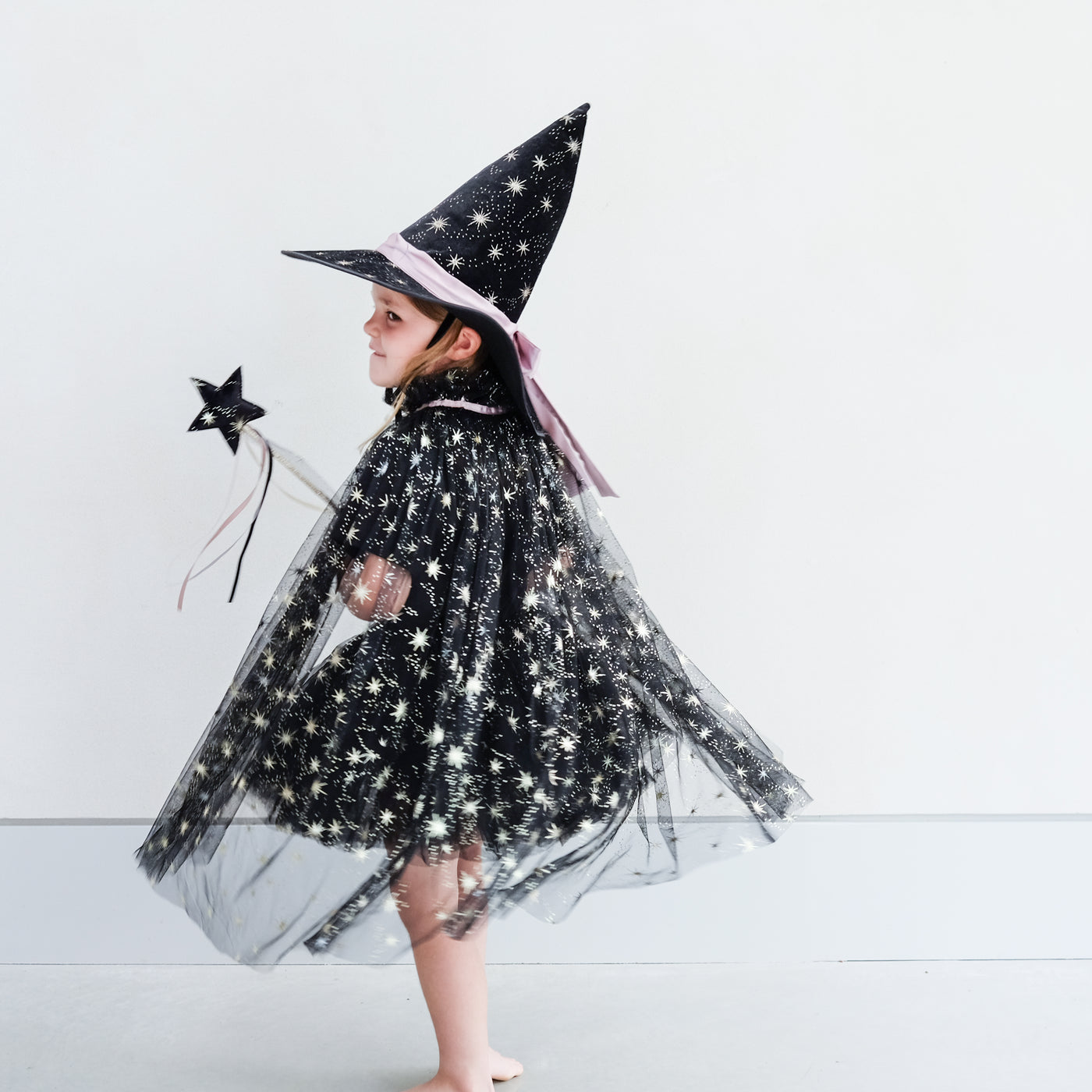 girl wearing black witches costume with gold foil star detail against a plain background