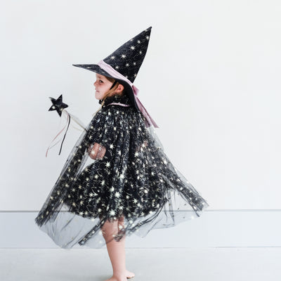girl wearing black witches costume with gold foil star detail against a plain background