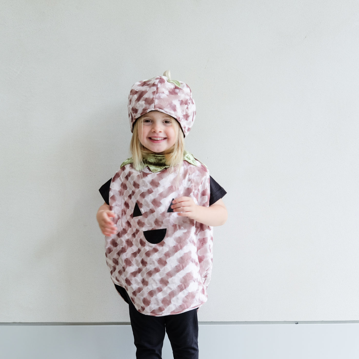 Child wearing a patterned pumpkin costume with a matching hat against a plain background