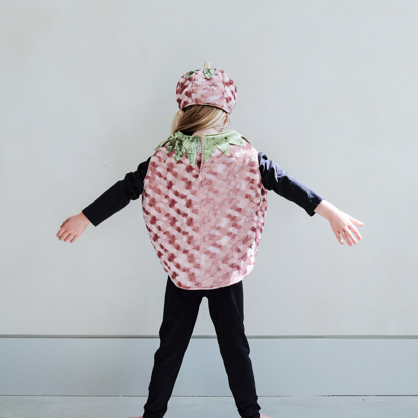Child wearing a patterned pumpkin costume with matching hat against a plain background