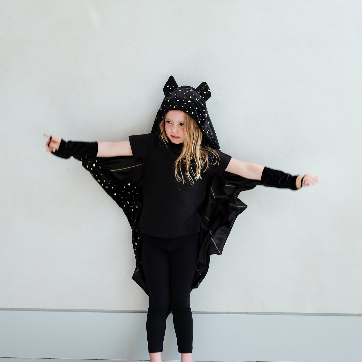 Child wearing a black bat costume with star details against a light grey background