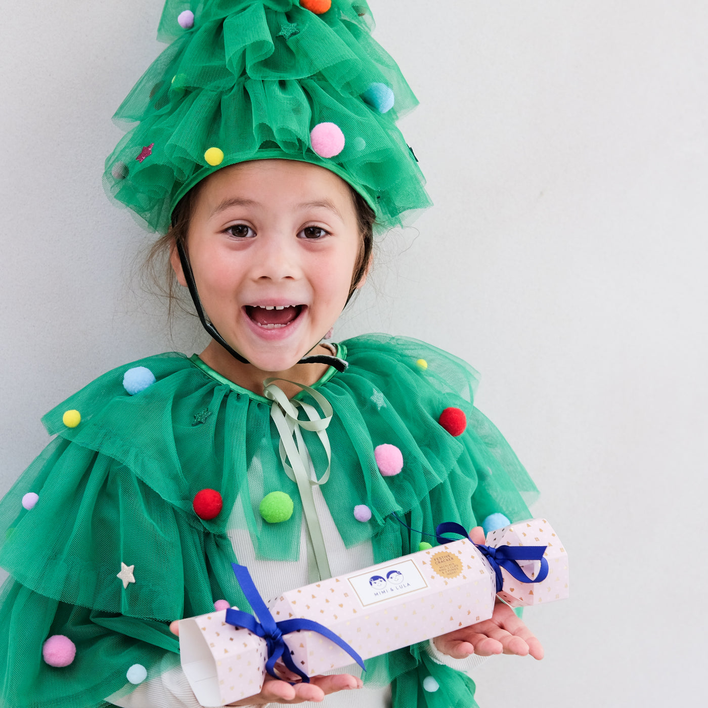 Child wearing a green Christmas tree costume holding a Christmas cracker gift box.