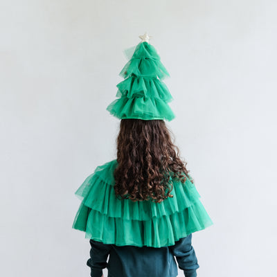 Child wearing a Christmas Tree costume with tulle and decorations, posing against a plain background.