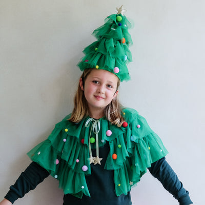 Child wearing a Christmas Tree costume with tulle and decorations, posing against a plain background.