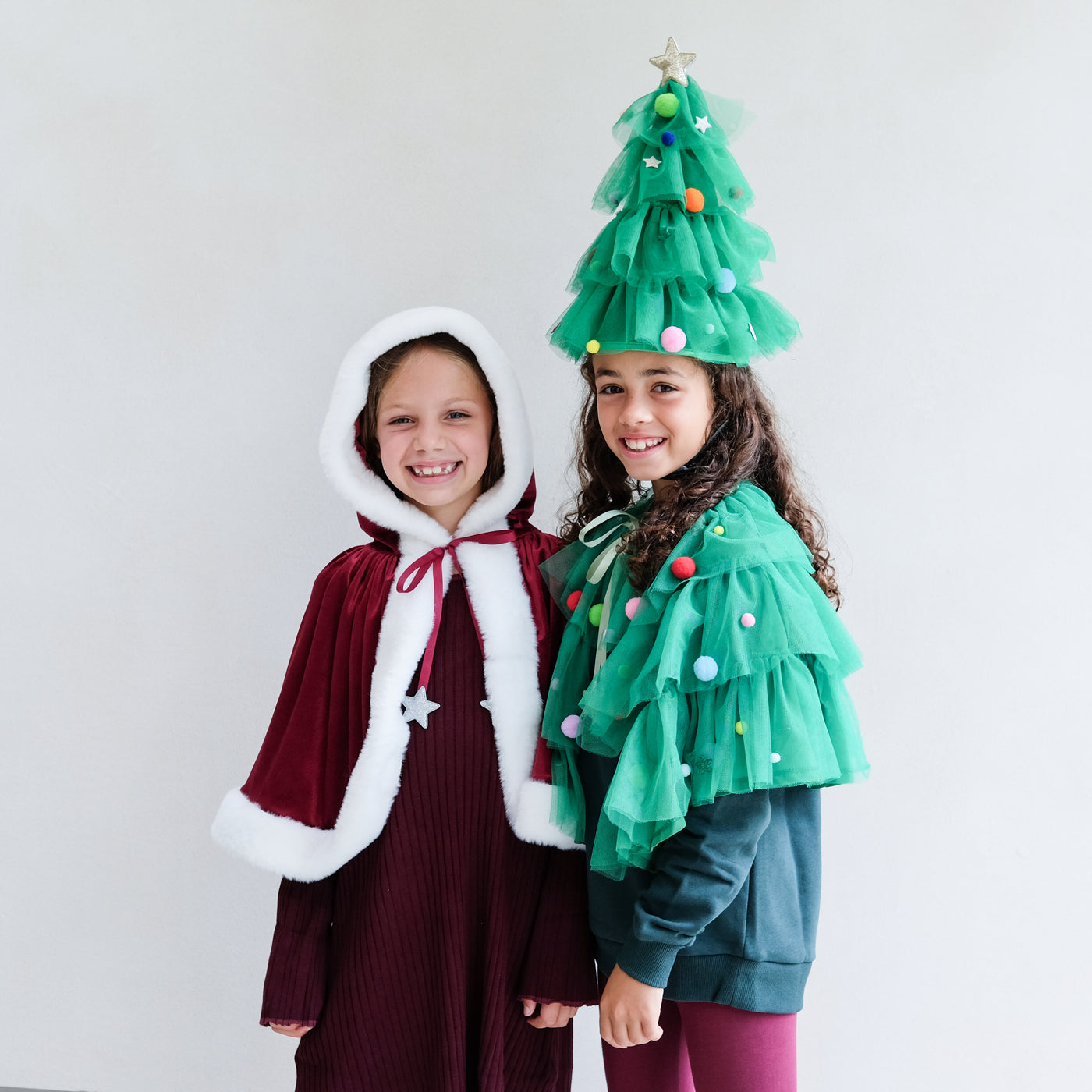 Two children wearing festive costumes, one resembling a Christmas tree, against a plain background.