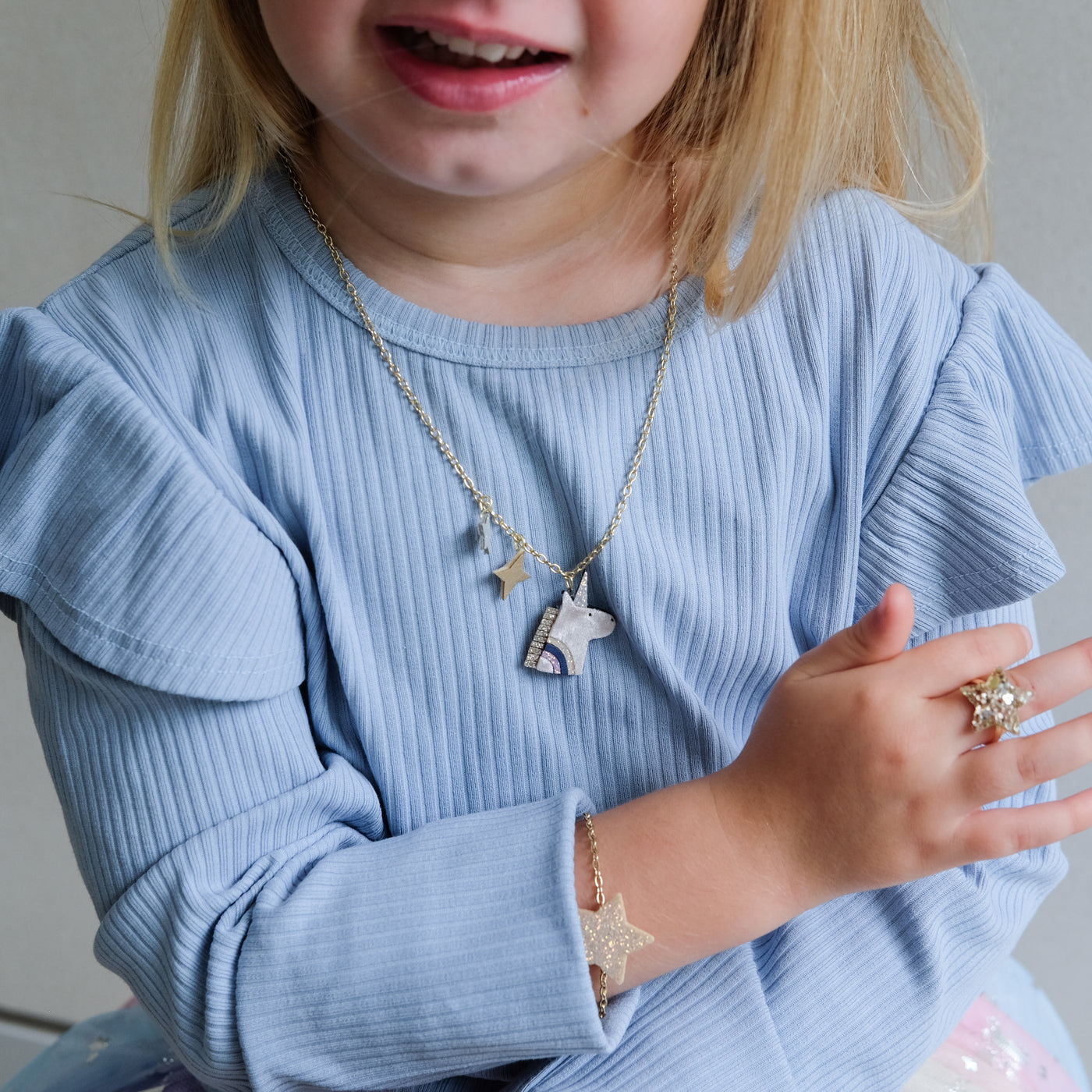 Child wearing a blue sweater with jewelry including a necklace, bracelet, and ring.