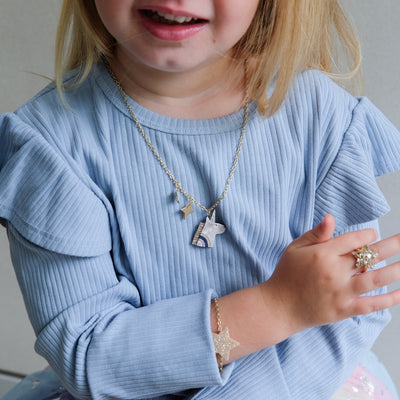 Child wearing a blue sweater with jewelry including a necklace, bracelet, and ring.