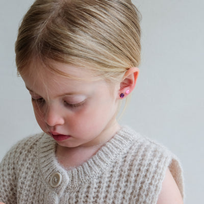 Young girl wearing a beige knitted cardigan and colourful earrings on a plain background