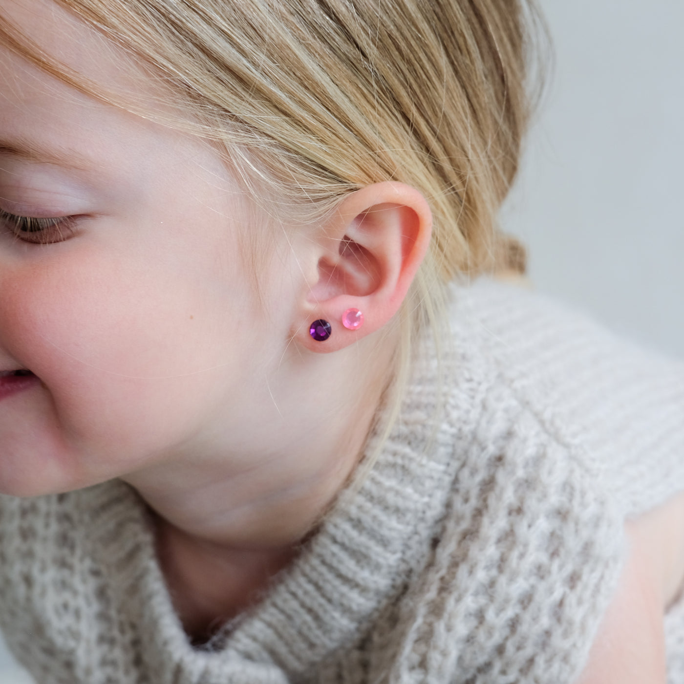 Close-up of a child wearing two small earrings on a plain background
