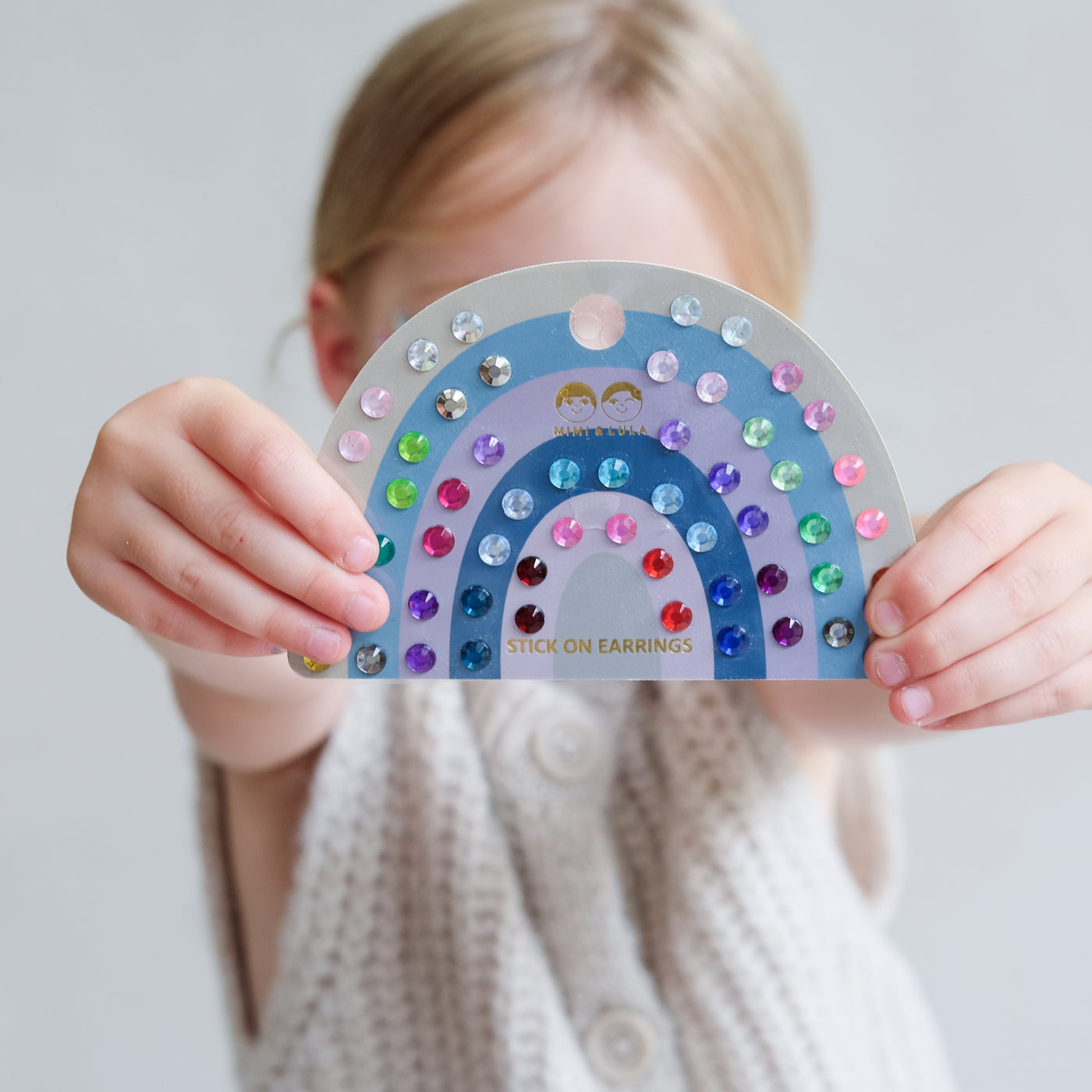 Child holding a rainbow-shaped earring kit with colourful beads