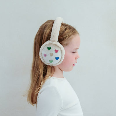 Child wearing fluffy earmuffs with colourful heart patterns on a plain background