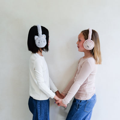Two children wearing fluffy earmuffs against a plain background