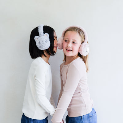 Two children wearing fluffy ear muffs against a plain background
