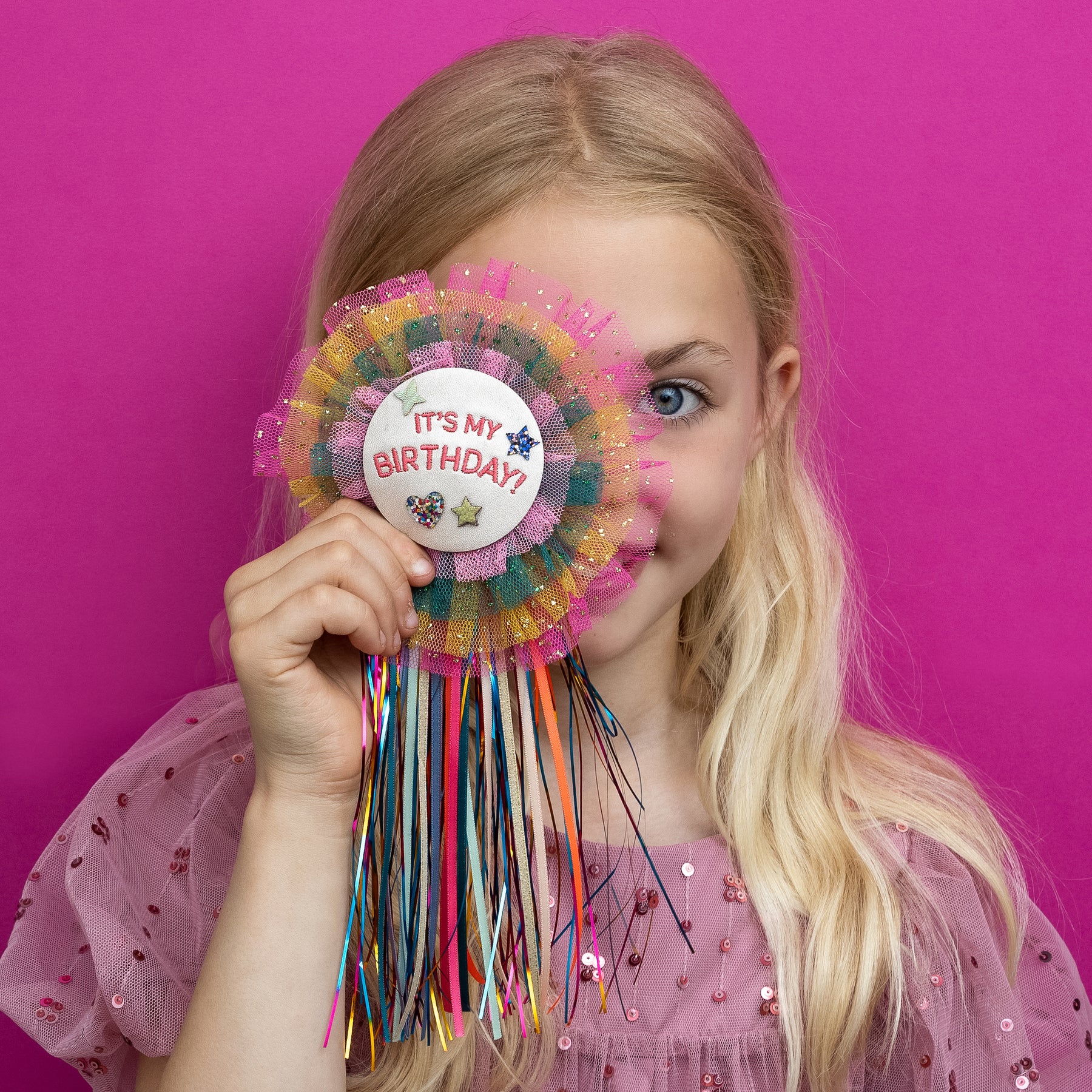 close up image of a vibrant rainbow birthday badge, bursting with a spectrum of bold colours, bold pink background, perfect for adding a cheerful touch to any celebration