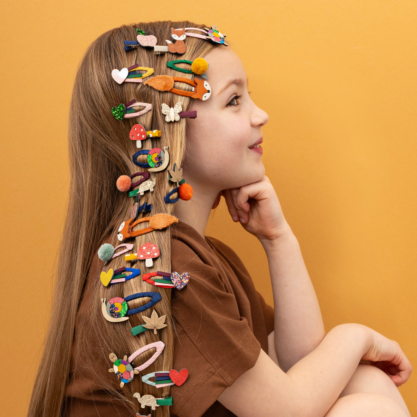 Little girl with hair down wearing many fun coloured hair clips, on a yellow background