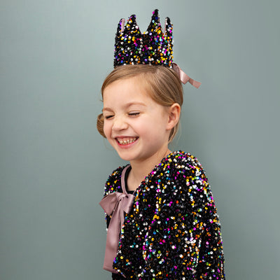 Little girl laughing wearing a sequin covered crown and cape with a satin pink tie