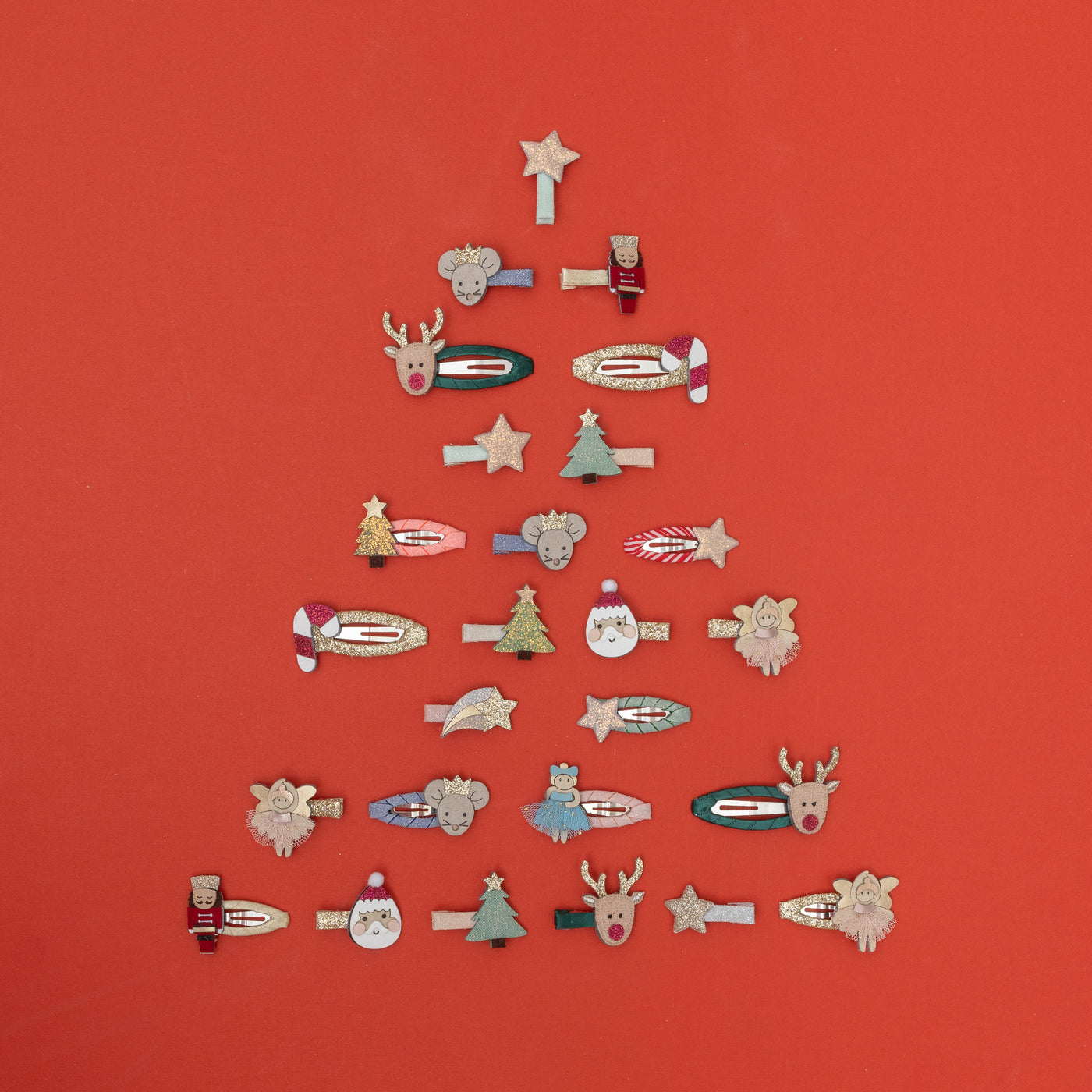 Beautiful assortment of children's mini hair clips placed on a red background in the shape of a Christmas tree, featuring nutcrackers, mice, reindeer, ballerinas, stars, santas, trees and candy canes
