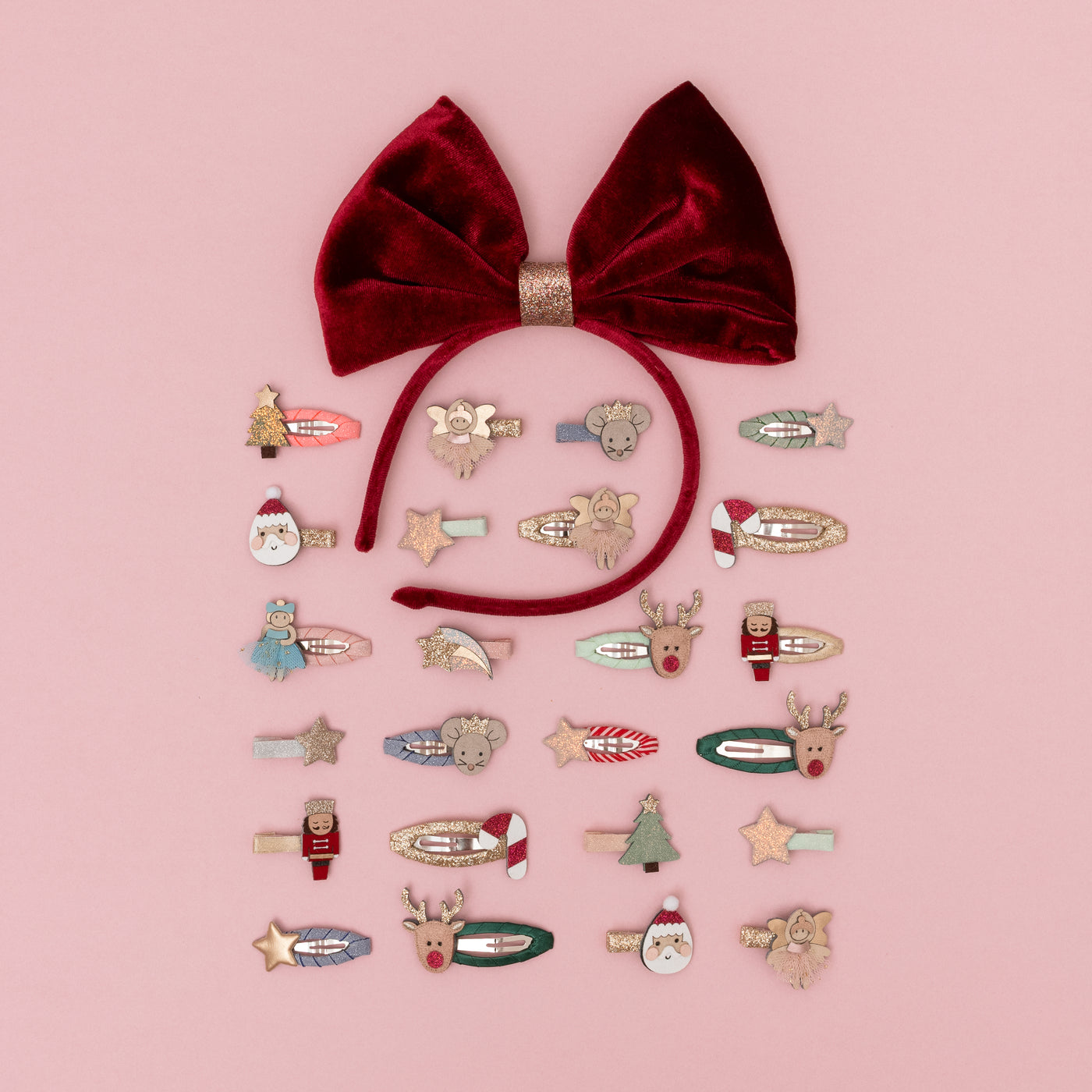 Oversize red velvet bow alice band on pink background arranged around a selection of Christmas themed mini clips for children