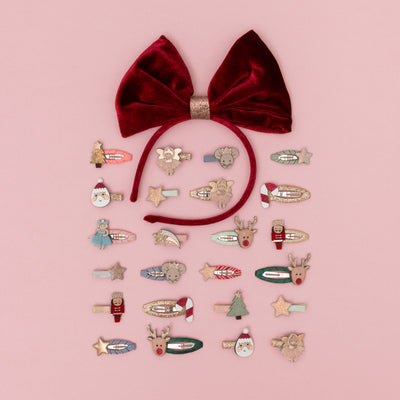 Oversize red velvet bow alice band on pink background arranged around a selection of Christmas themed mini clips for children
