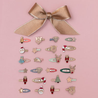Assortment of children's Christmas themed mini hair clips placed on a pink background - includes nutcrackers, ballerinas, mice, santas, candy canes, stars, and trees