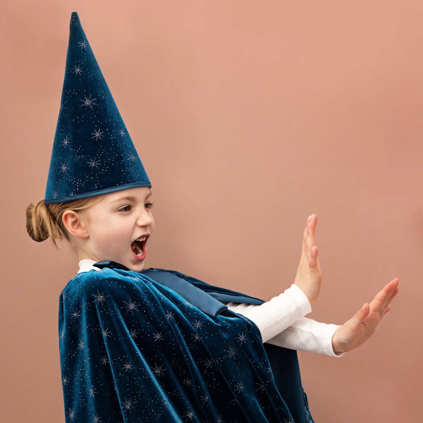 Little girl playing wearing a deep teal velvet cape embellished with stars and matching conical wizard hat