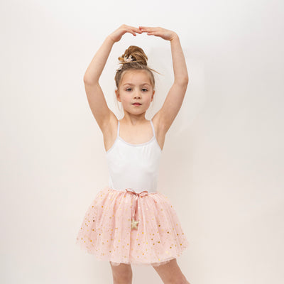 Little girl in a ballet pose wearing a pretty pink tulle tutu speckled with golden stars and ballet inspired hair clips