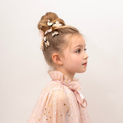 Little girl wearing a soft tulle gold star speckled cape with hair tied up in a bun decorated with ballet theme hair clips and bows