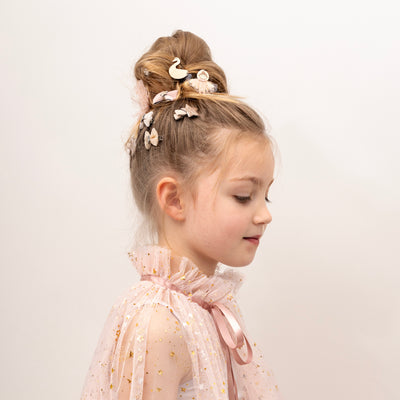 Little dark blonde girl with hair up in a bun decorated with ballet theme hair clips, looking downwards