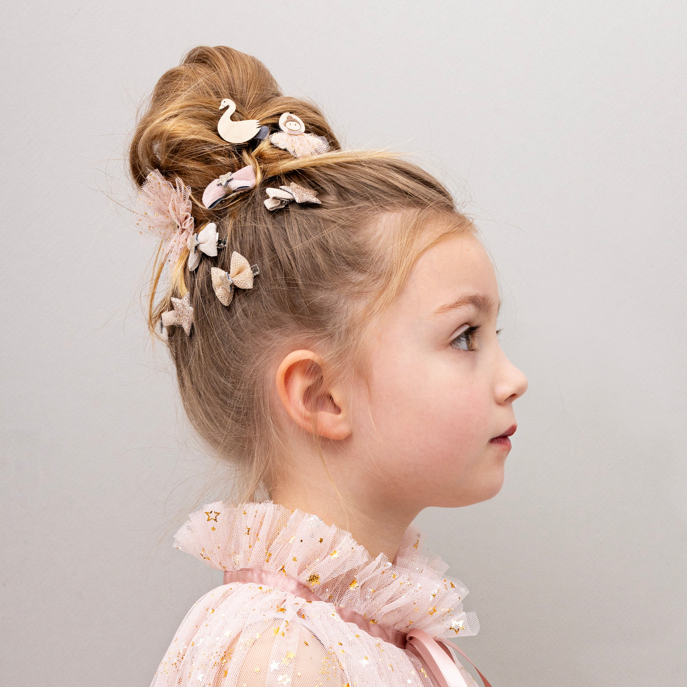 Little girl with hair up in a bun wearing a pretty pink tulle cape and hairclips featuring bows, stars and ballet dancers