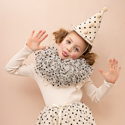 Little girl dressed as a clown in matching polka dot white and cream tulle tutu, ruffle collar and conical hat with pom poms