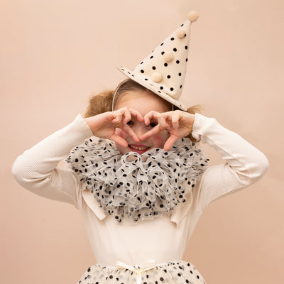 Little girl making a heart shape with her hands and peeping through whilst wearing a polka dot ruffle tulle clown collar and matching hat