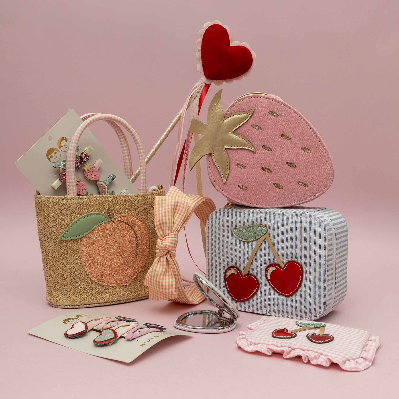 Set of children's accessories including a pink strawberry-shaped bag, peach basket bag, and cherry-themed items on a pink background.