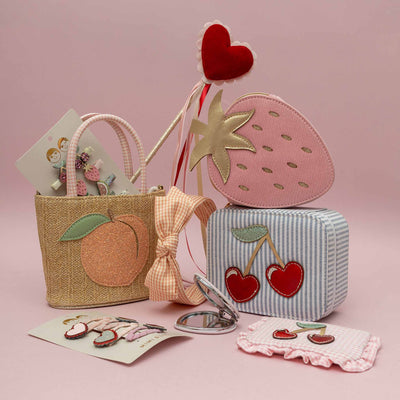 Set of children's accessories including a pink strawberry-shaped bag, peach basket bag, and cherry-themed items on a pink background.