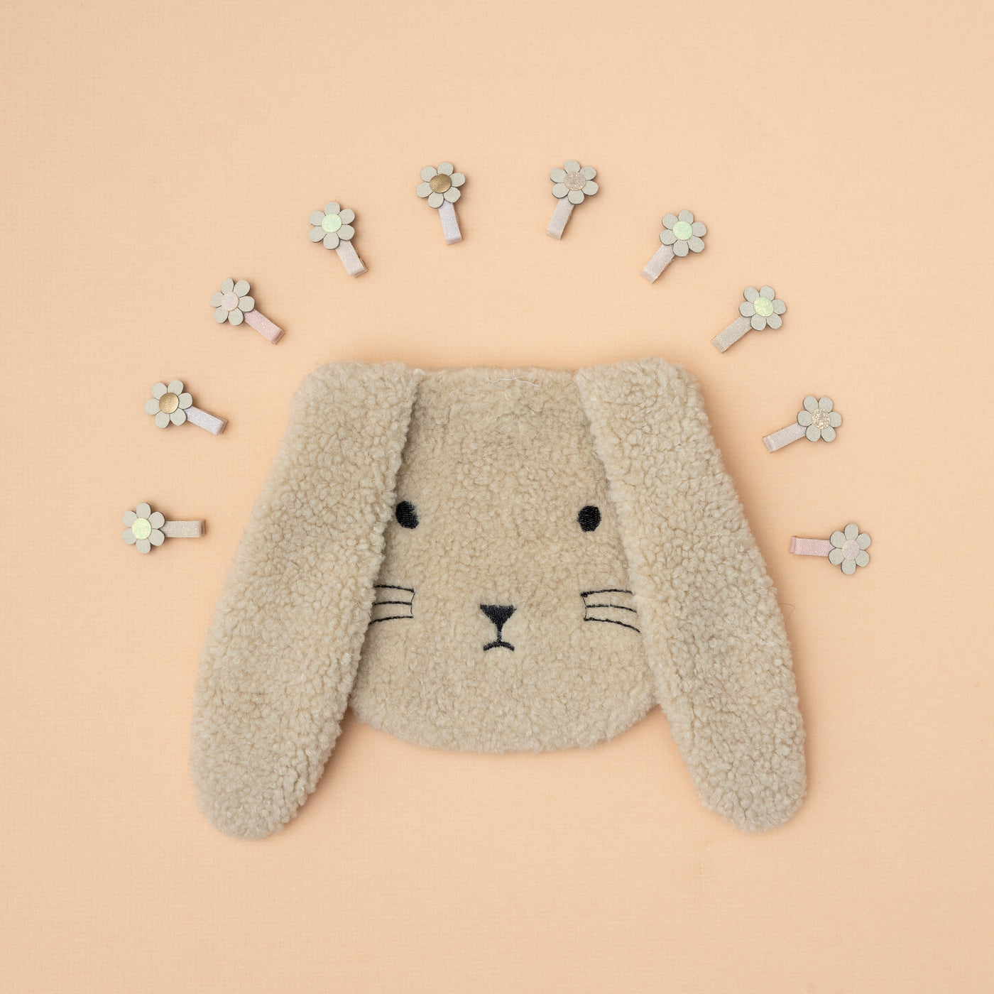 Fluffy bunny rabbit face bag surrounded by mini daisy hair clips laid on a peach / neutral background