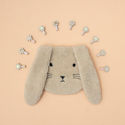 Fluffy bunny rabbit face bag surrounded by mini daisy hair clips laid on a peach / neutral background