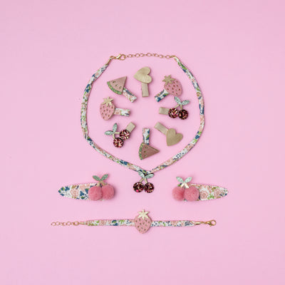 Fruit jewellery set laid on a pink background with lots of fruit themed hair clips