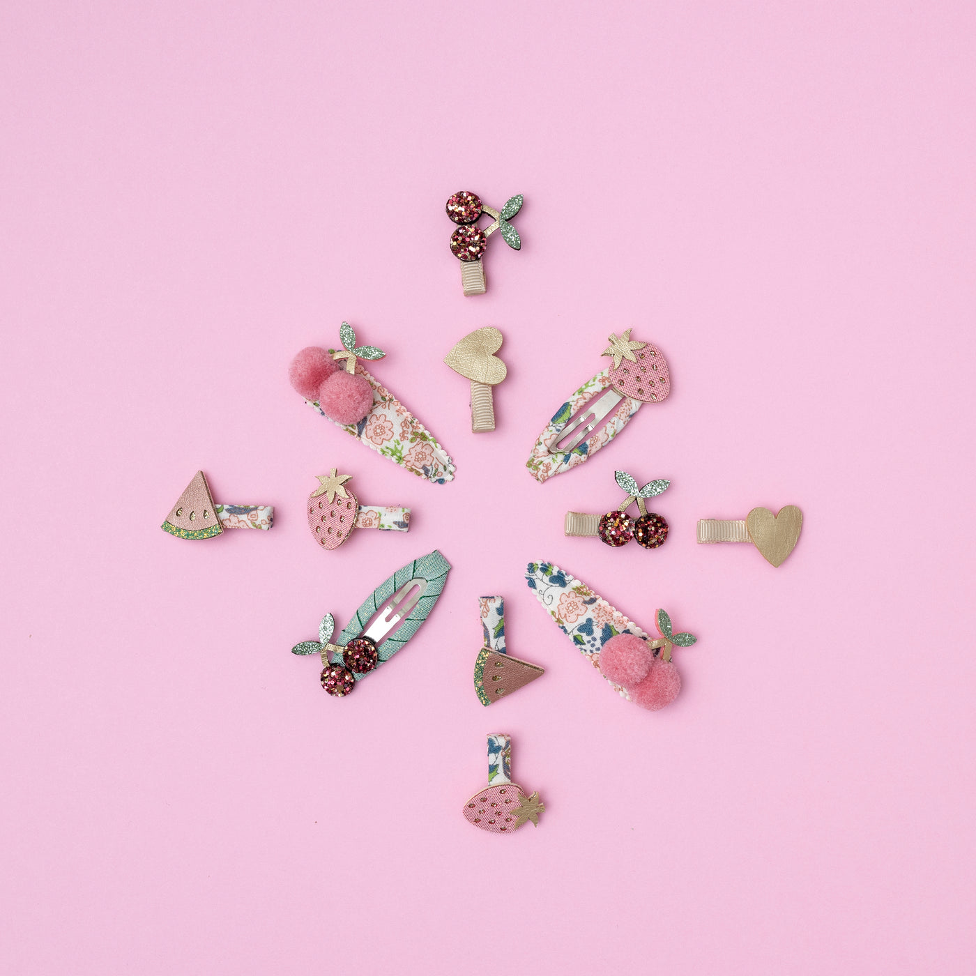 Fruit and floral themed hair clips arranged on a pink background