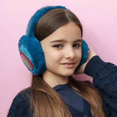 Dark haired girl smiling on pink background wearing colourful rainbow earmuffs with soft, fluffy padding, designed to keep little ears warm and cosy