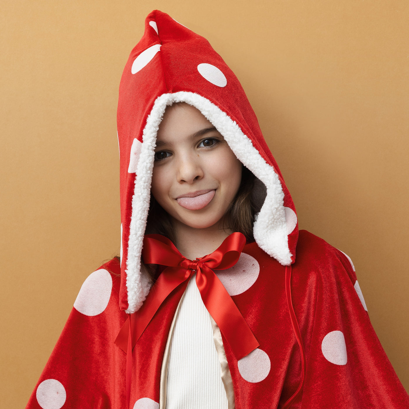 Little girl wearing a toadstool dress up set featuring red sateen hat with white spots, fluffy borg lining, borg pompoms-Red velvet cape with white spots- gold lining- Red sateen ribbon closure