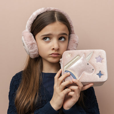 Dark haired girl looking up holding a blush pink velvet unicorn box bag- zip closure- cross body strap- glittery unicorn  and star detail and wearing matching pale pink fluffy unicorn design earmuffs